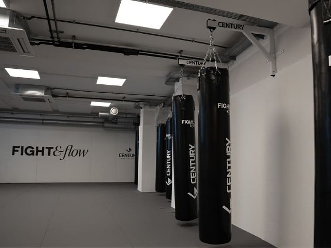 Reihe schwarzer Boxsäcke im Fight Room, an der Wand das Studio-Logo
